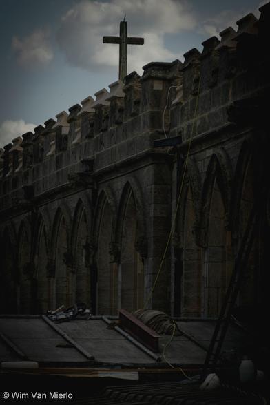 A dark view of the exterior of the church nave viewed from the rooftop. A crucifix on top of the nave.