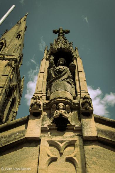 Stone carvings and stone statue on the church rooftop, with church's spire and a metal rod from scaffolding.