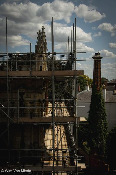 Church rooftop with scaffolding in the sunlight, with blue sky under white clouds.