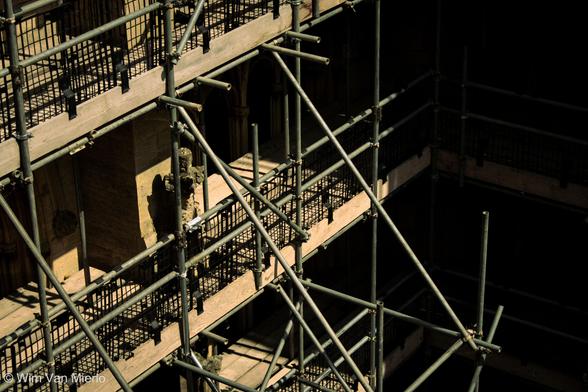 Detail view of scaffolding around the side of a church in bright sunlight, with heavy shadows.