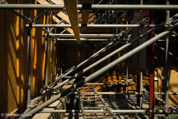 Inside scaffolding, showing various diagonal and horizontal steel pipes and supports that are surrounded by a plywood encasing.