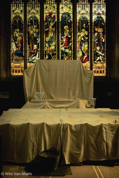 Interior of the church: side altar covered in white sheets to protect it from grime in front of a colourful stained-glass window.
