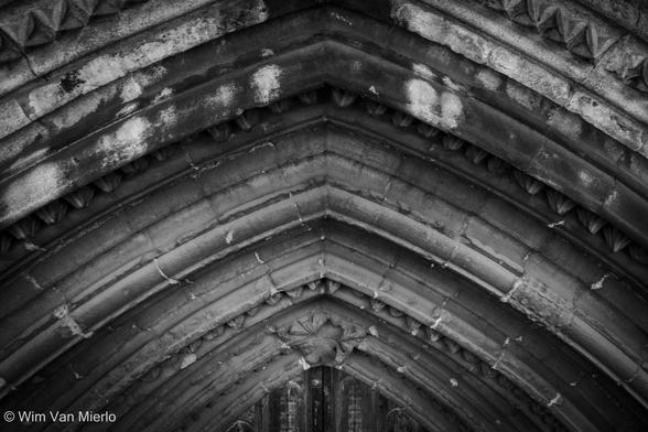 Black and white image with a detail of stone masonry above an arched church door.