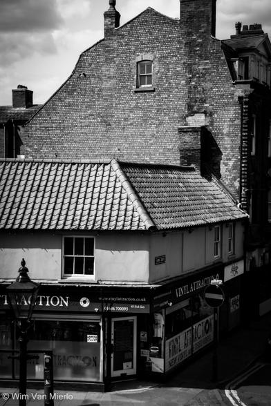 Black and white image of brick houses and a shop at street level on the street corner.