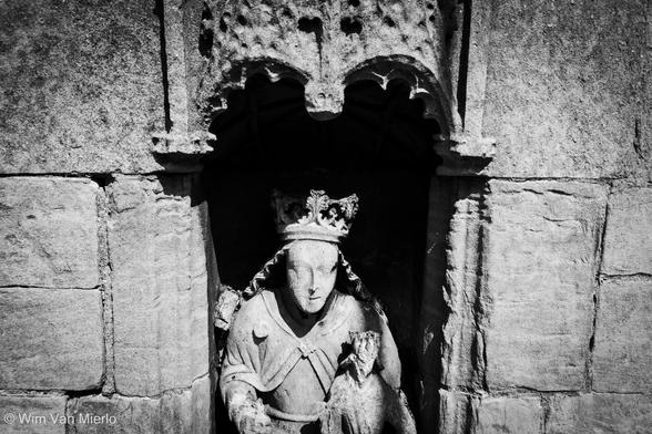 Black and white image of a stone-carved statue in a niche in the wall of a church, presumably the image of the Virgin Mary.