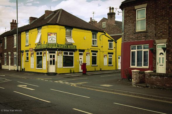 A house with the 'Tasty Bites' cafe painted bright yellow on the corner of an empty road.
