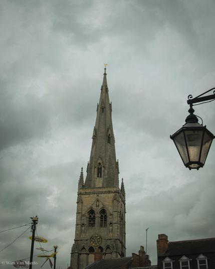 A church spire rising above the houses.  Tightly cropped, a street lantern hangs from the right.