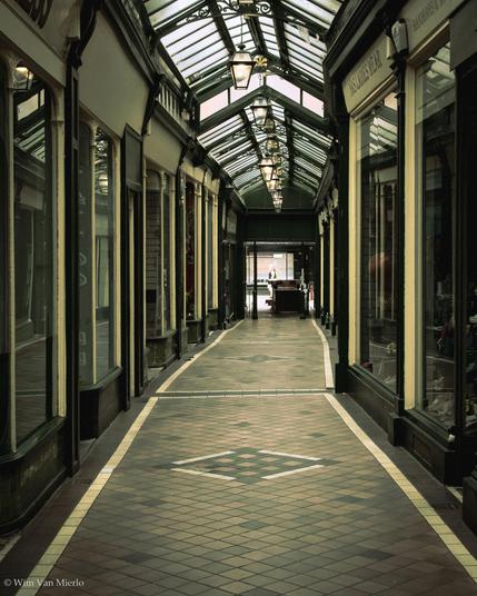 An empty shopping arcade passage with a row of lanterns hanging from the glass roof.