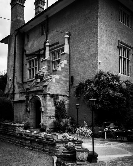 Black and white image of a stately manor, showing a side entrance.