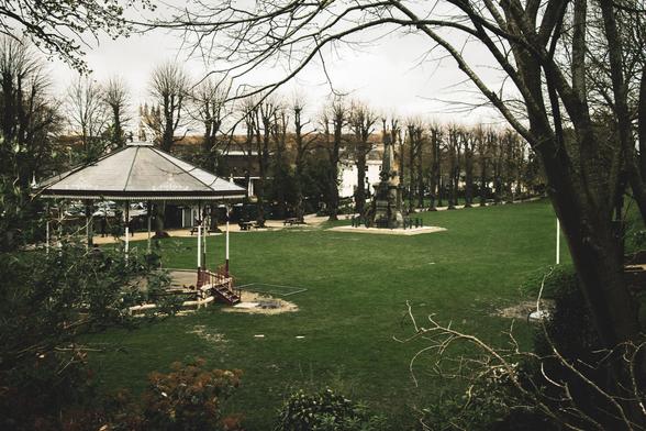 Photography of a park: gazebo, line of trees, grass field, grey sky.  The angle is from slightly higher up looking downwards.