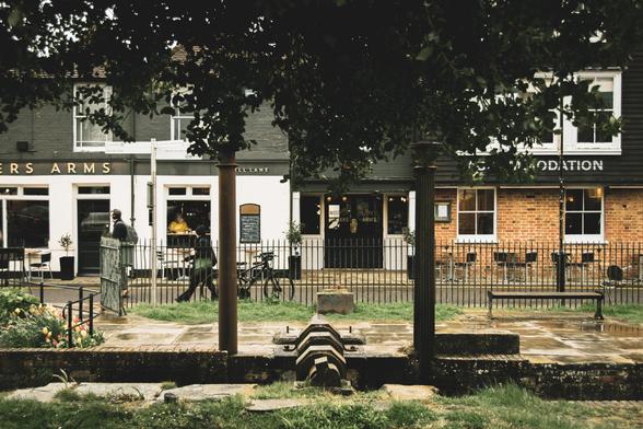 Photograph: behind the trees two people walk in front of a pub.