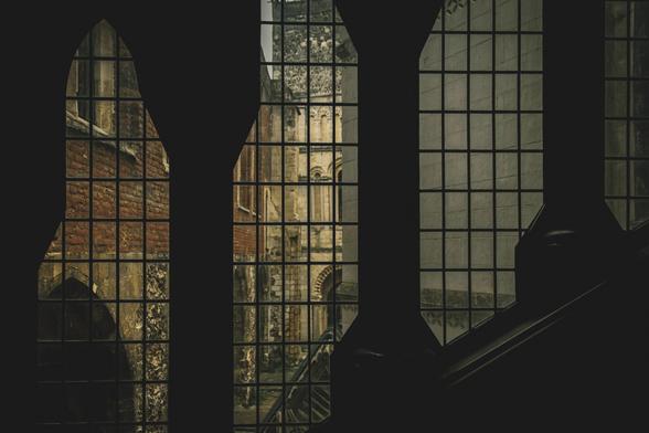 A dark image: a window with dark columns looking to an exterior scene of a small courtyard.