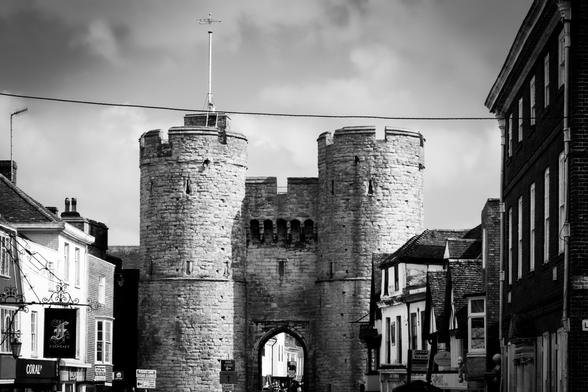Black and white photograph of a medieval gate with round towers in an old city.