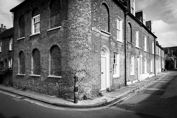 Black and white photograph on a street corner: old, birck buildings in the sunlight.
