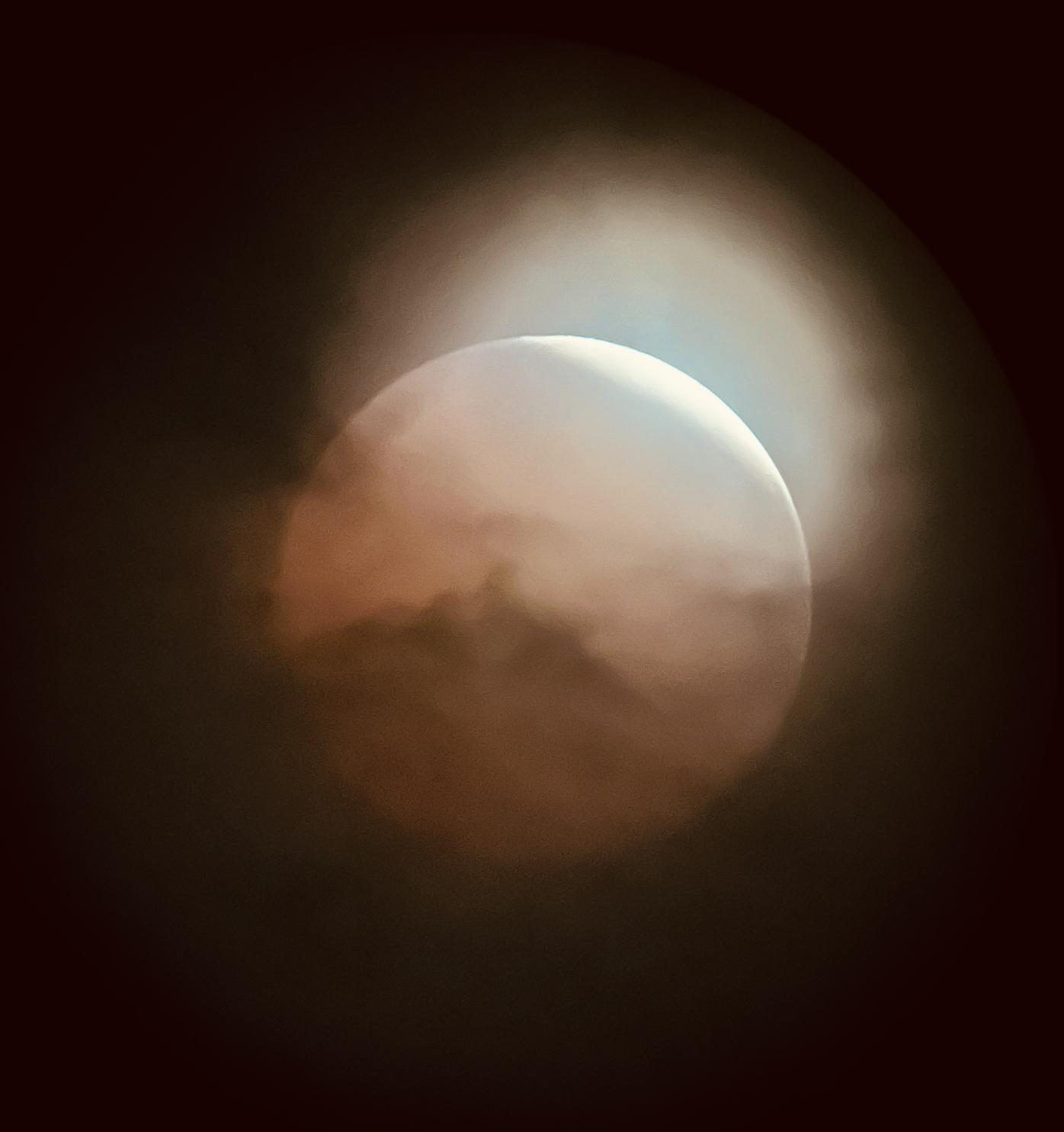 A close-up picture of the full moon, partially obscured by the clouds, and reddened by the Earth's shadow.